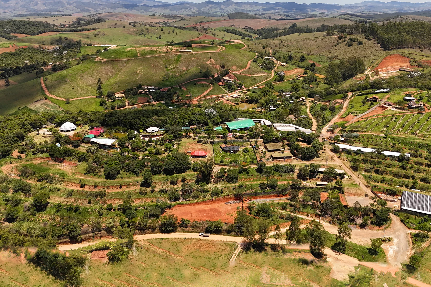 Vista aérea atual da Aldeia Outro Mundo, mostrando as diversas bioconstruções, domos, áreas de reflorestamento e o sistema de energia solar.