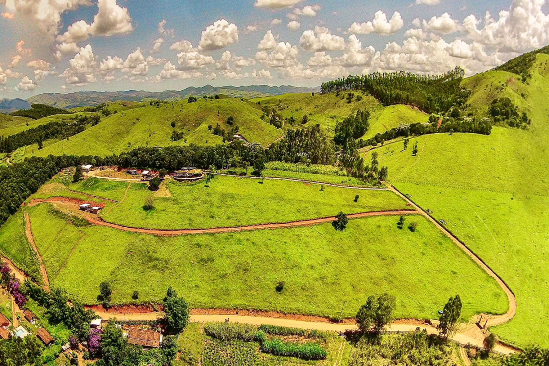 Vista aérea panorâmica do terreno da Aldeia Outro Mundo em seu início, mostrando as colinas verdes e poucas construções em Lagoinha, SP.