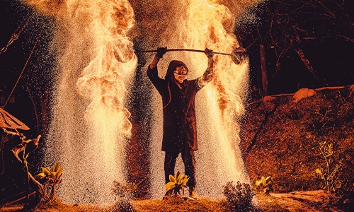 Artista performático com bastões de fogo criando efeitos de faíscas intensas, iluminando a noite durante um evento ou festival na Aldeia Outro Mundo.